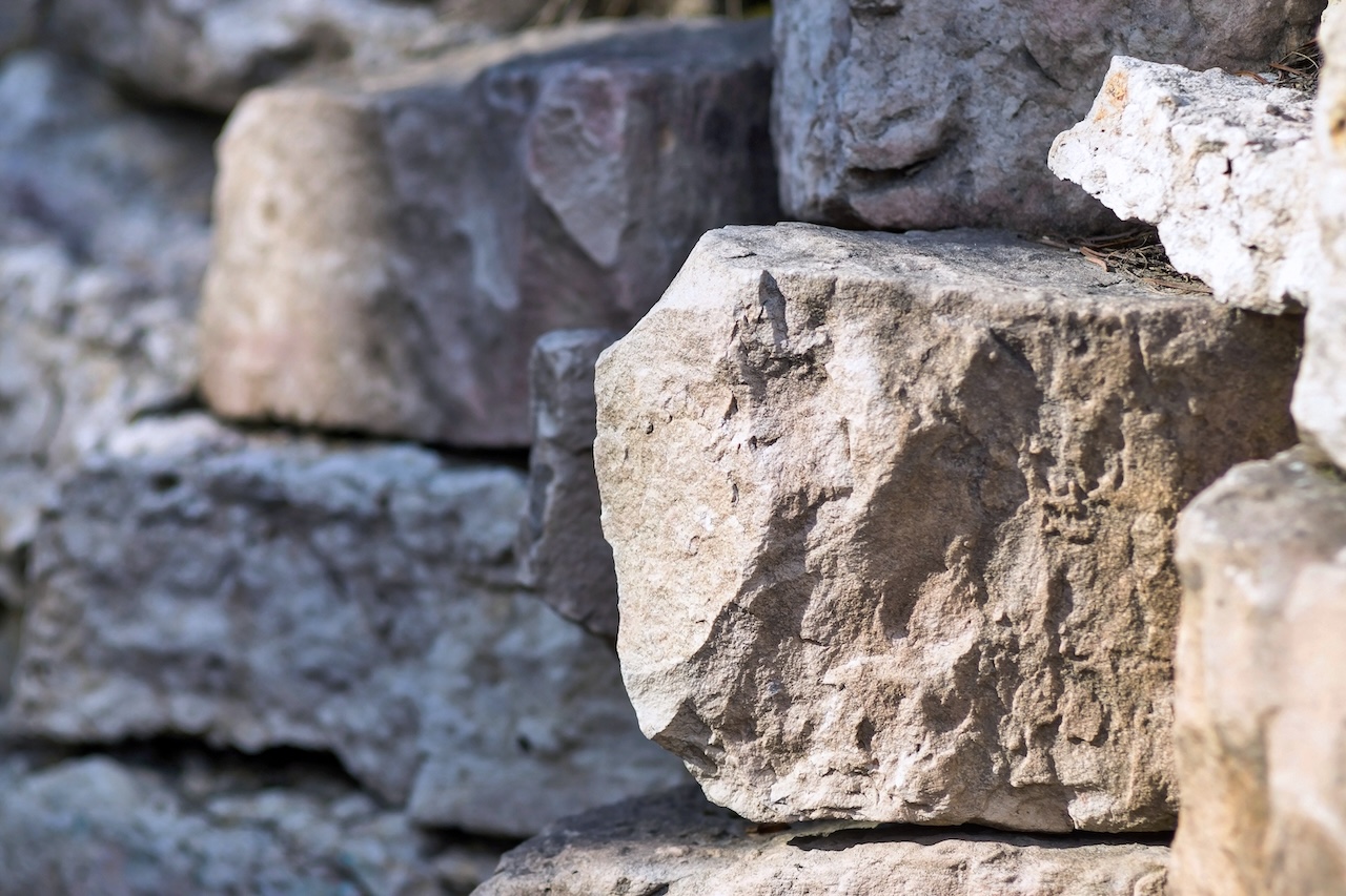 big piece of a stone closeup on an indistinct background from other stones Learn how wall stone supports retaining walls, slope stabilization, and landscape construction projects while improving durability, drainage, and curb appeal in large-scale outdoor installations.